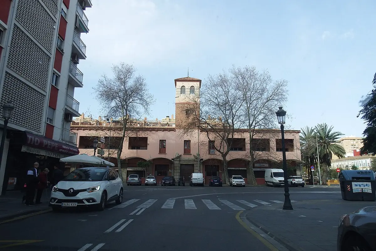 Městská tržnice Cabanyal ve Valencii, nízká růžová budova s malou věží, viděná přes ulici s platanovými stromy